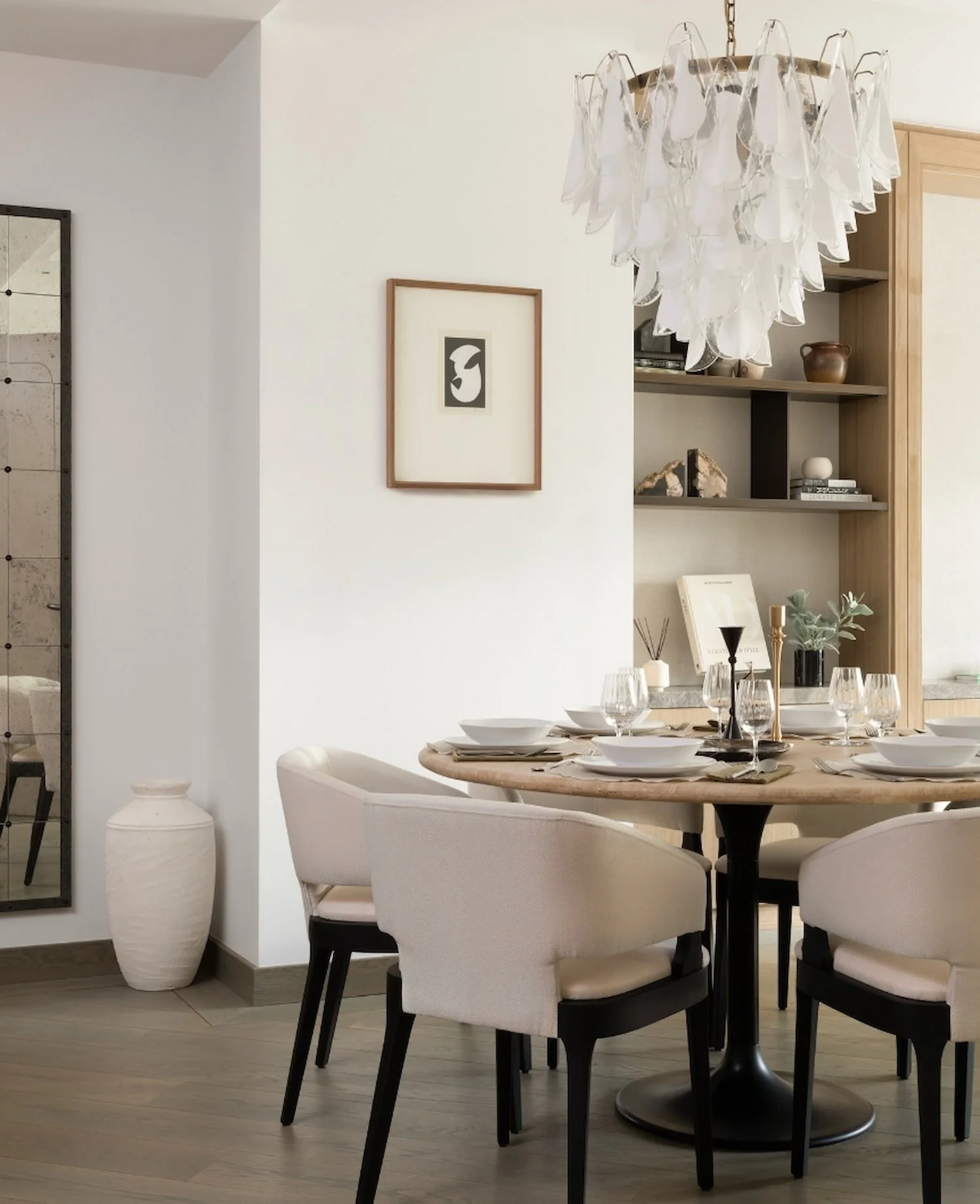 Elegant dining room featuring a round oak table with white chairs and a bespoke glass petal chandelier by Abigail Reay