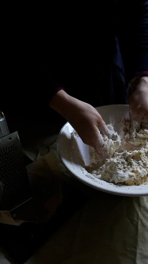 Hands rubbing cold grated butter into white flour in a ceramic bowl to create a breadcrumb texture for mince pie pastry
