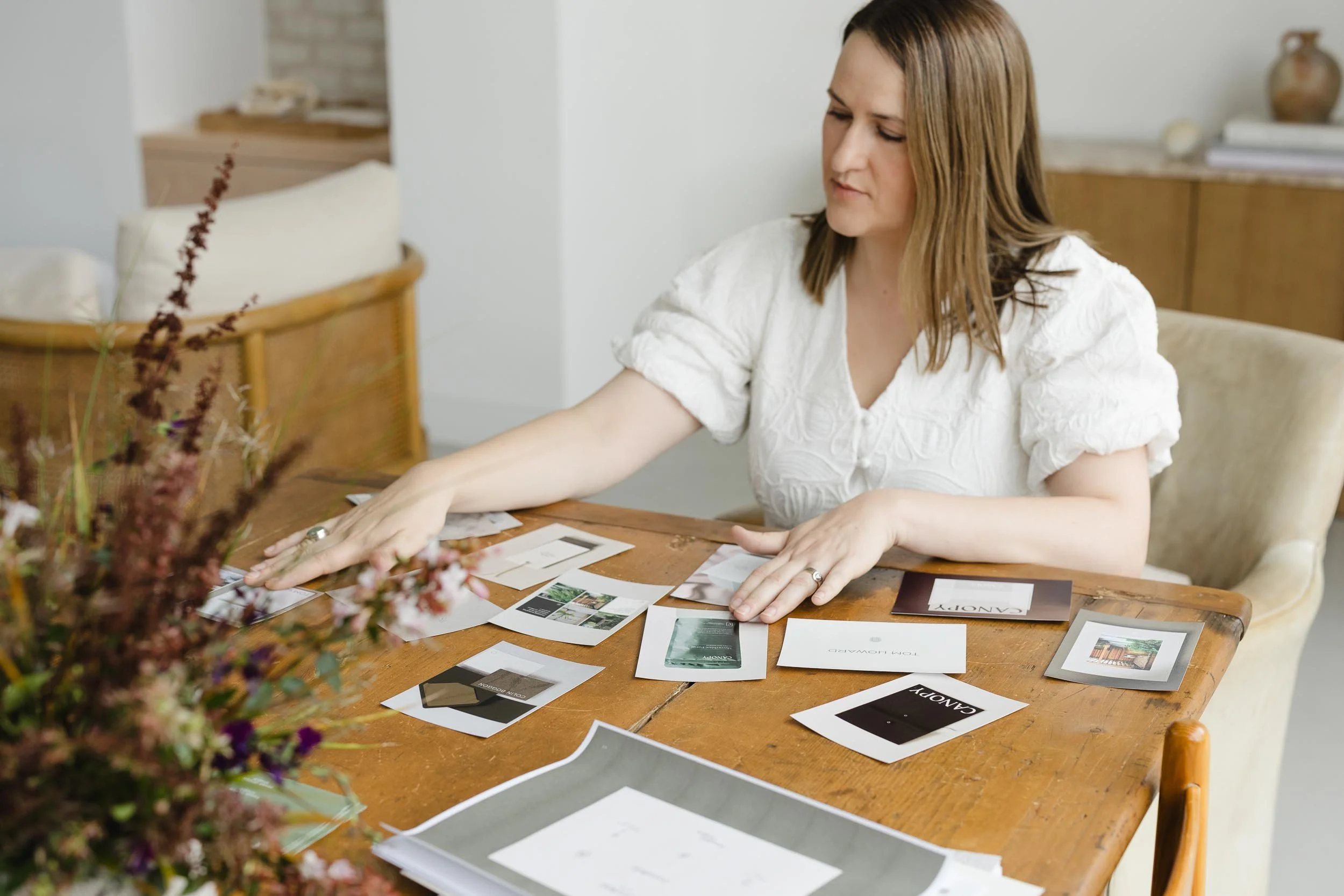 Designer at a wooden table reviewing printed brand identity concepts for garden design plus lifestyle business projects