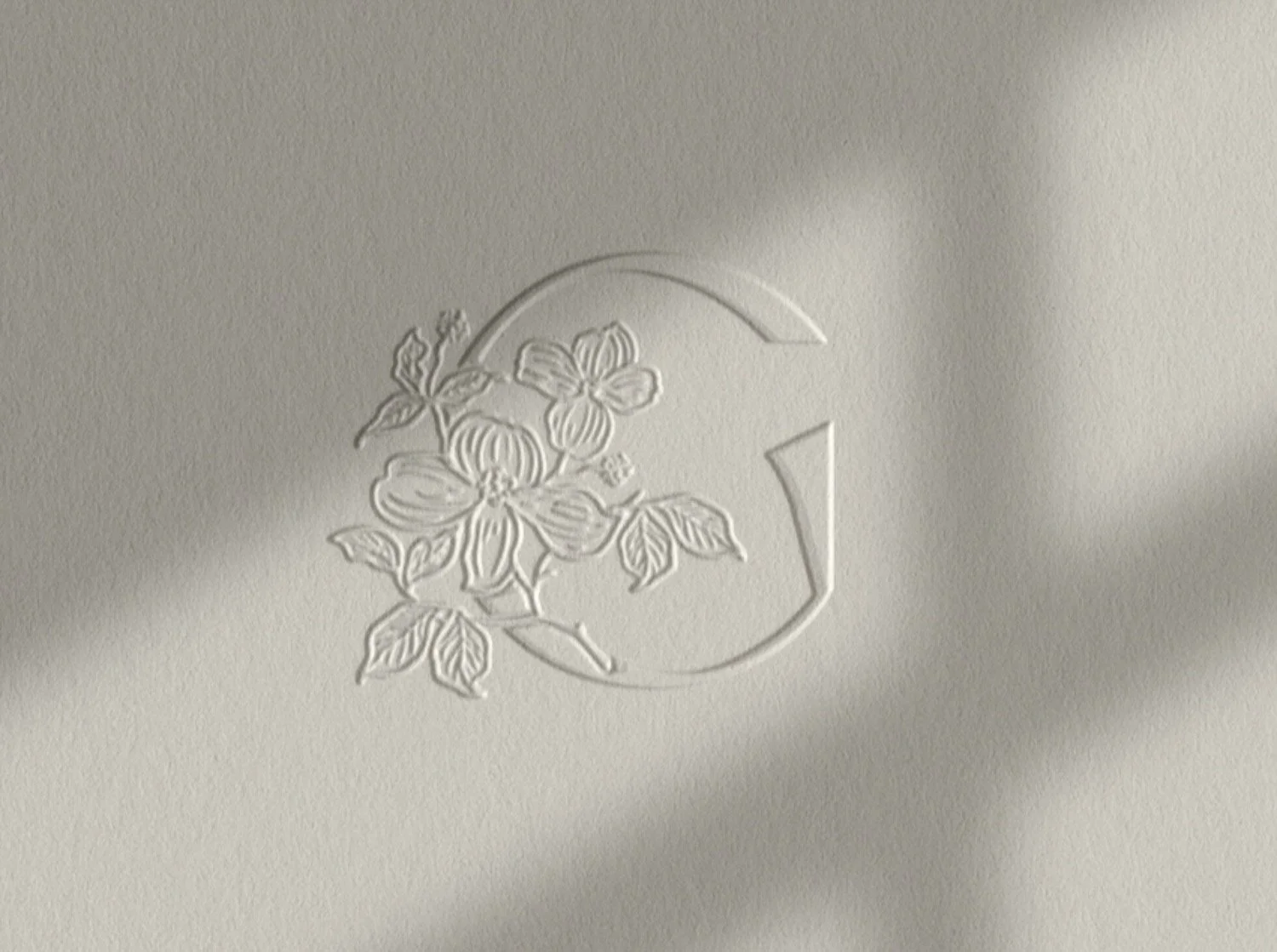 High-end brand mark featuring a floral illustration intertwined with a debossed G monogram on cream textured paper