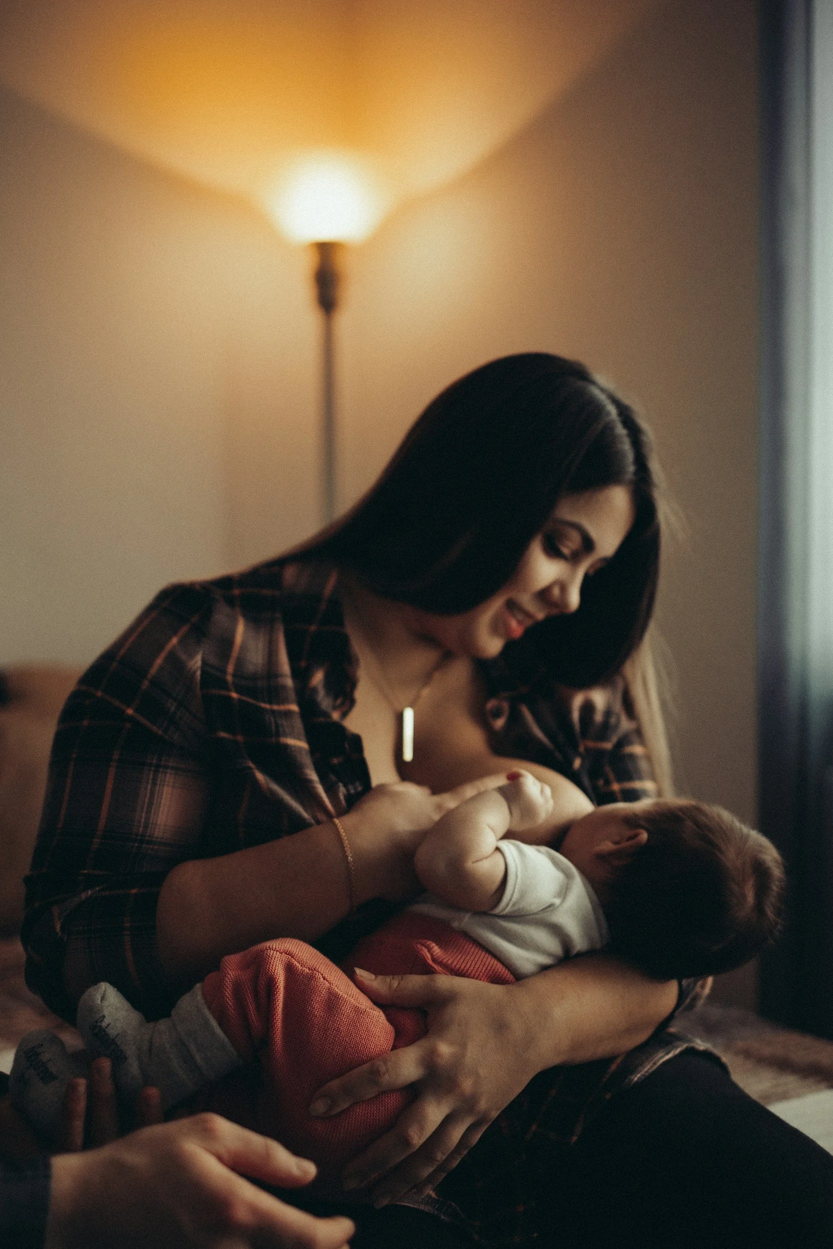 breastfeeding mother and baby in a living room with a standing lamp behind her