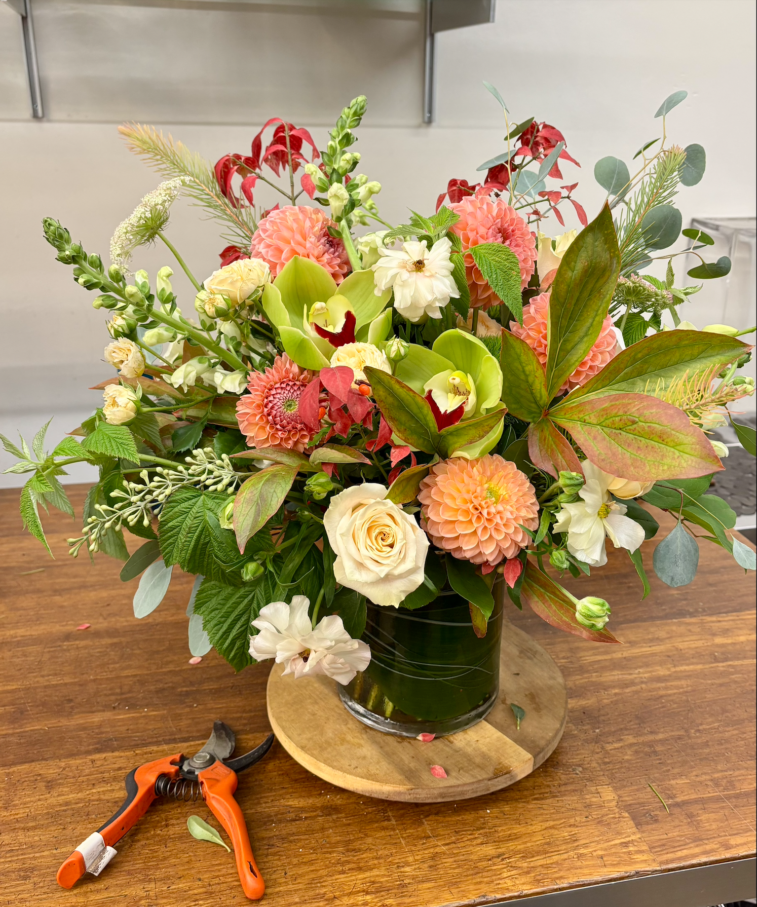 A colorful flower arrangement in a black vase on a wooden table, with pruning shears nearby.