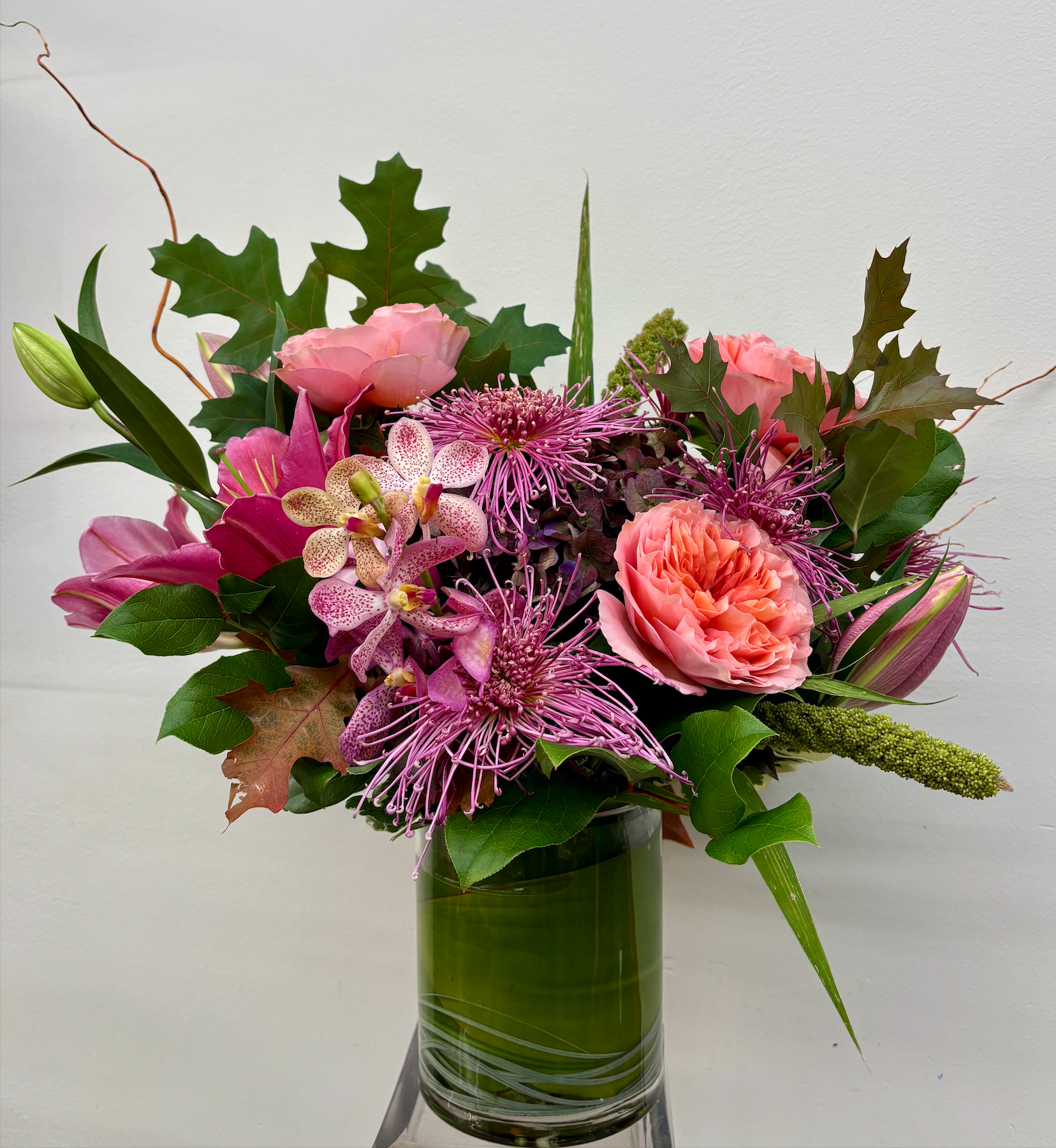 A floral arrangement in a green glass vase with various pink, purple, and green flowers and leaves.
