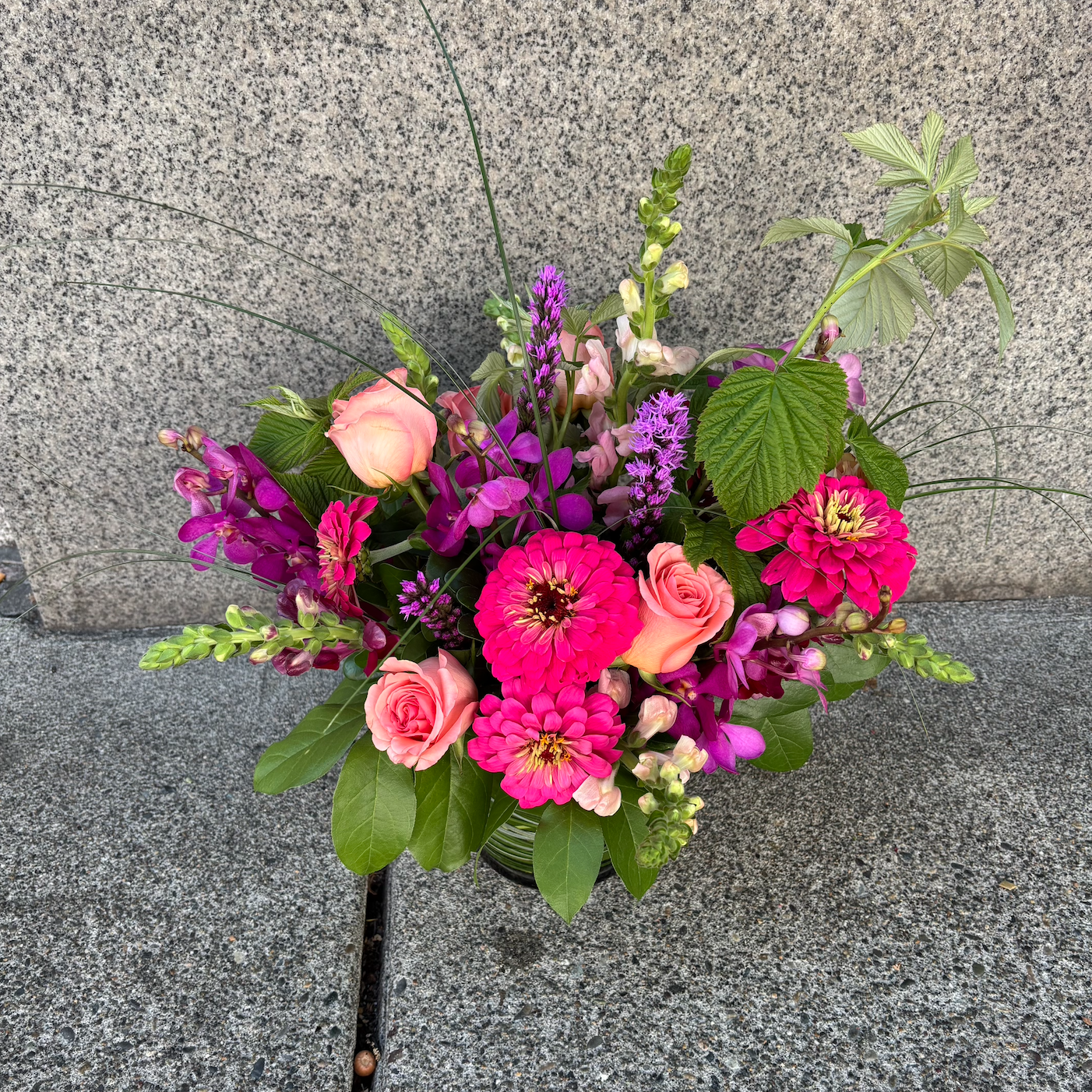 Vase of mixed pink, purple, and peach flowers on a stone surface.