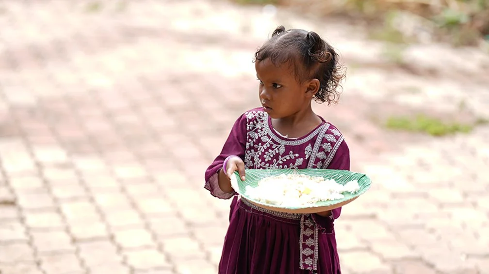 a young girl carries a large bowl of cooked rice