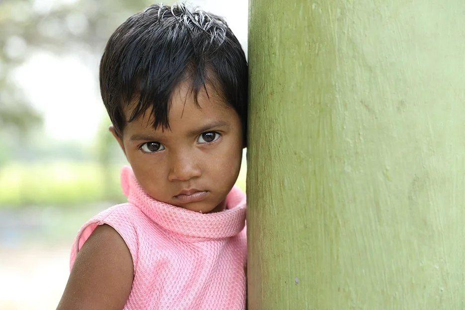 A young girl in south asia leans agains a post