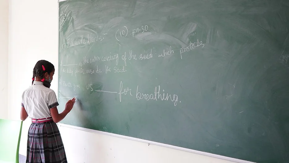 A girl in a school uniform writes on a blackboard