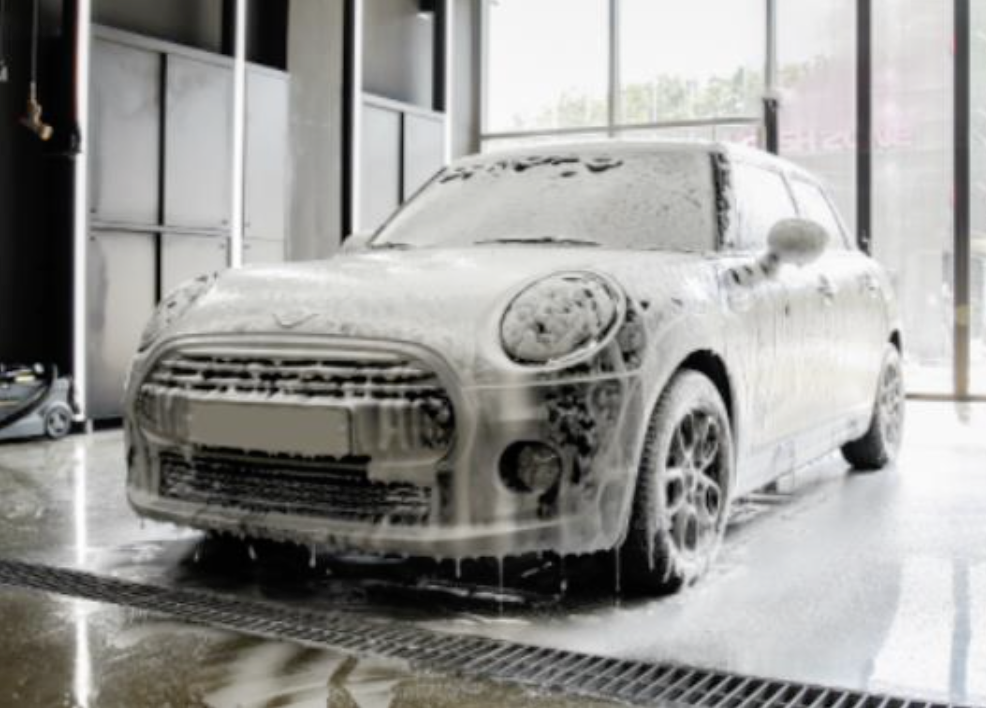 A Mini Cooper covered in foam soap during a car wash inside a garage.