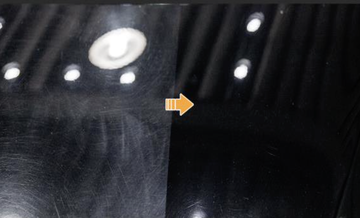 Close-up of a black baseboard heater showing small white circular control knobs and an orange arrow pointing from the top knob to the bottom right corner.