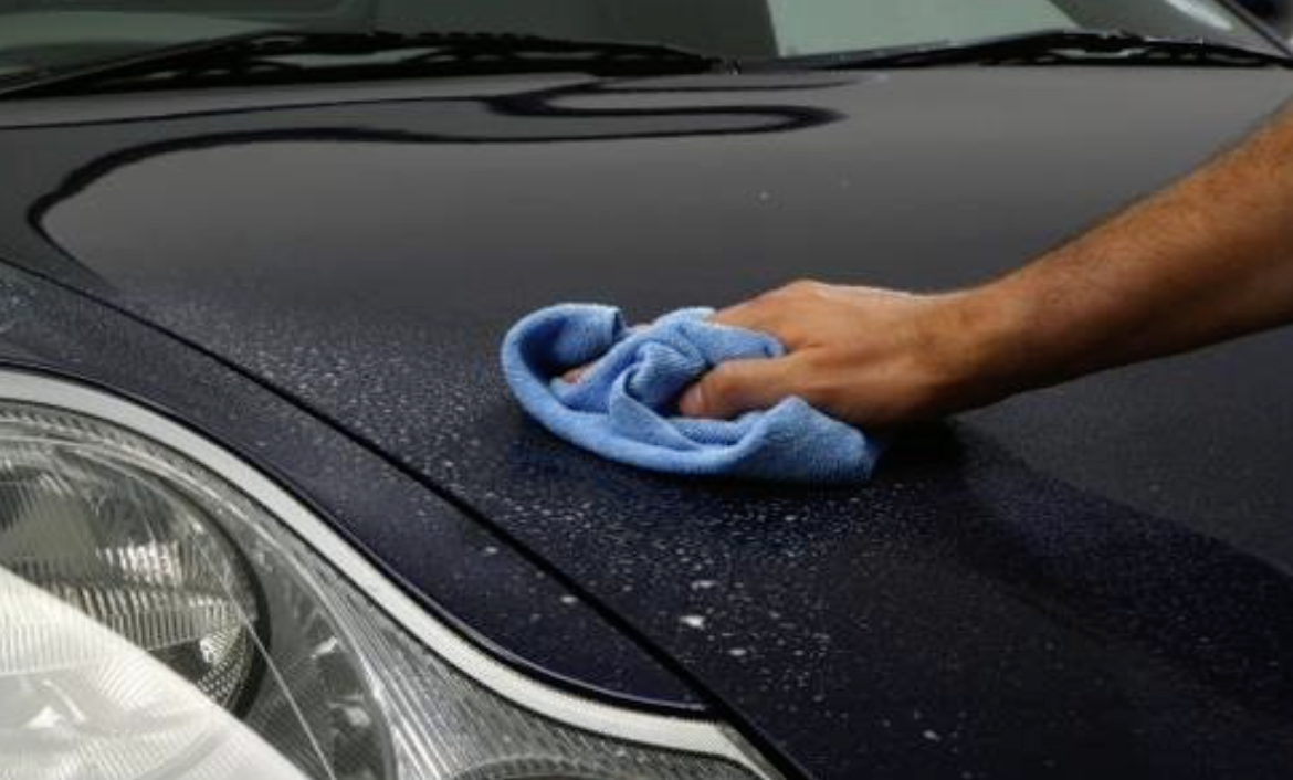A person wiping a black car's hood with a blue cloth.