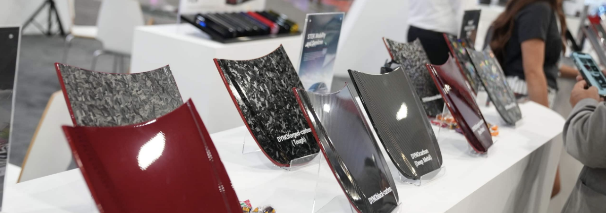 Display of various textured and colored materials or panels on a white table at an exhibition or show.