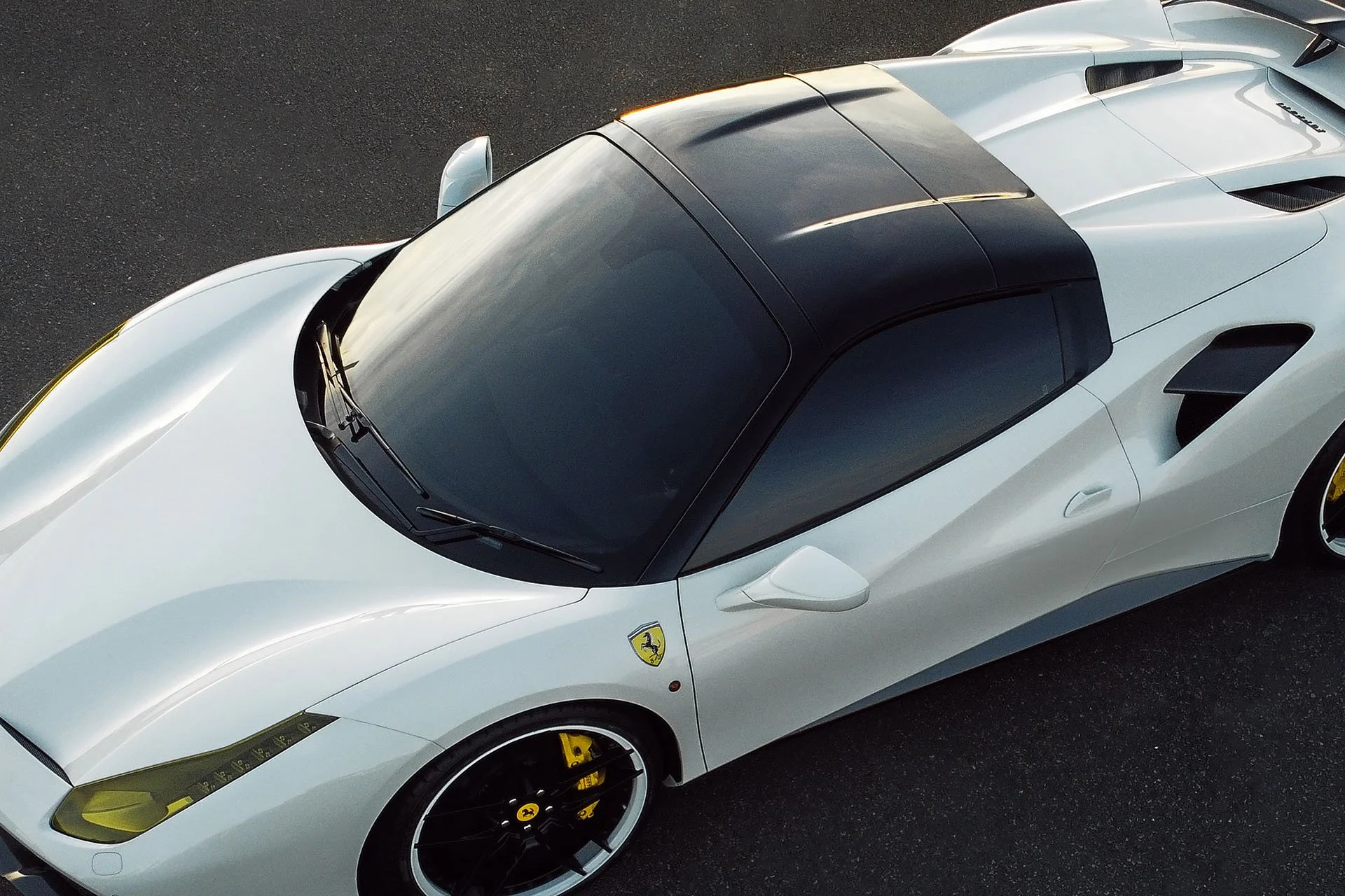 Top view of a white Ferrari sports car with a black roof, parked on asphalt.
