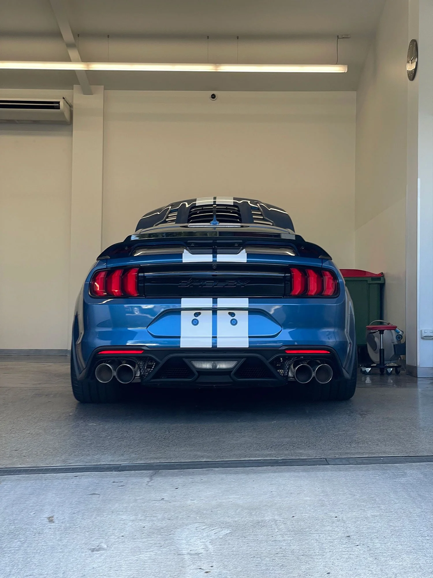 Rear view of a blue Ford Mustang Shelby GT with racing stripes in a garage.