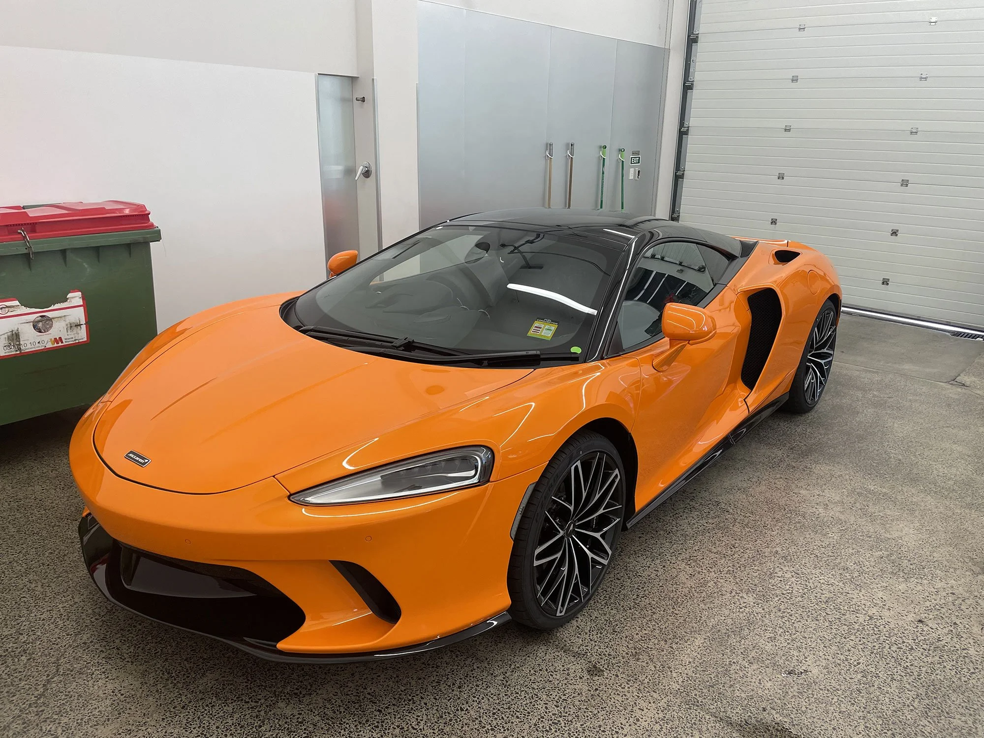 An orange sports car parked inside a garage. The car has a sleek, modern design with black wheels and a black roof.