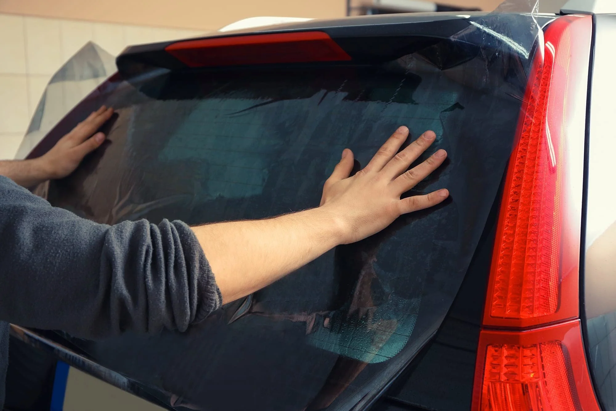 Person applying a black vinyl wrap to the back of a car.