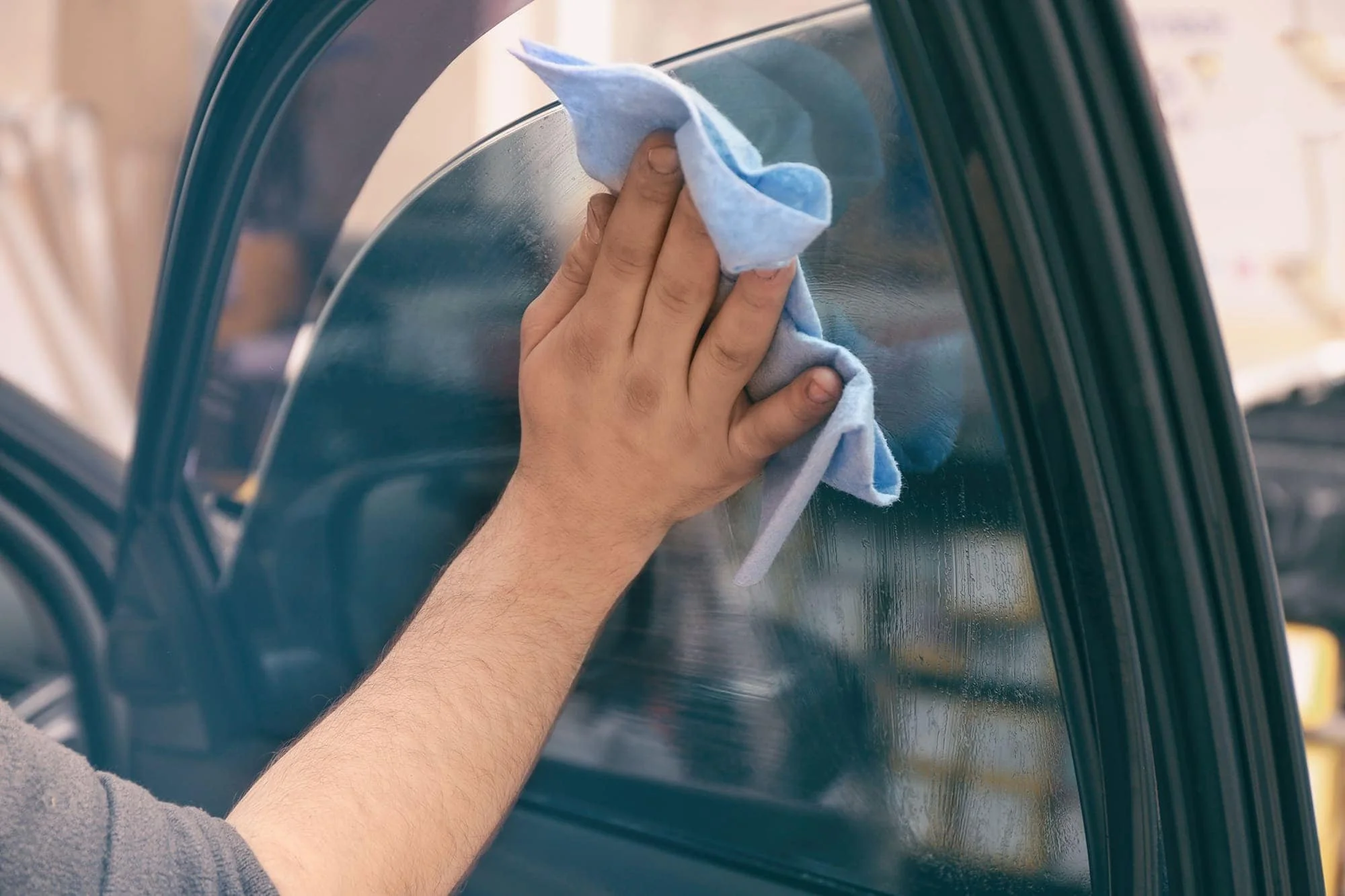 A person cleaning the glass window of a washing machine with a blue cloth.