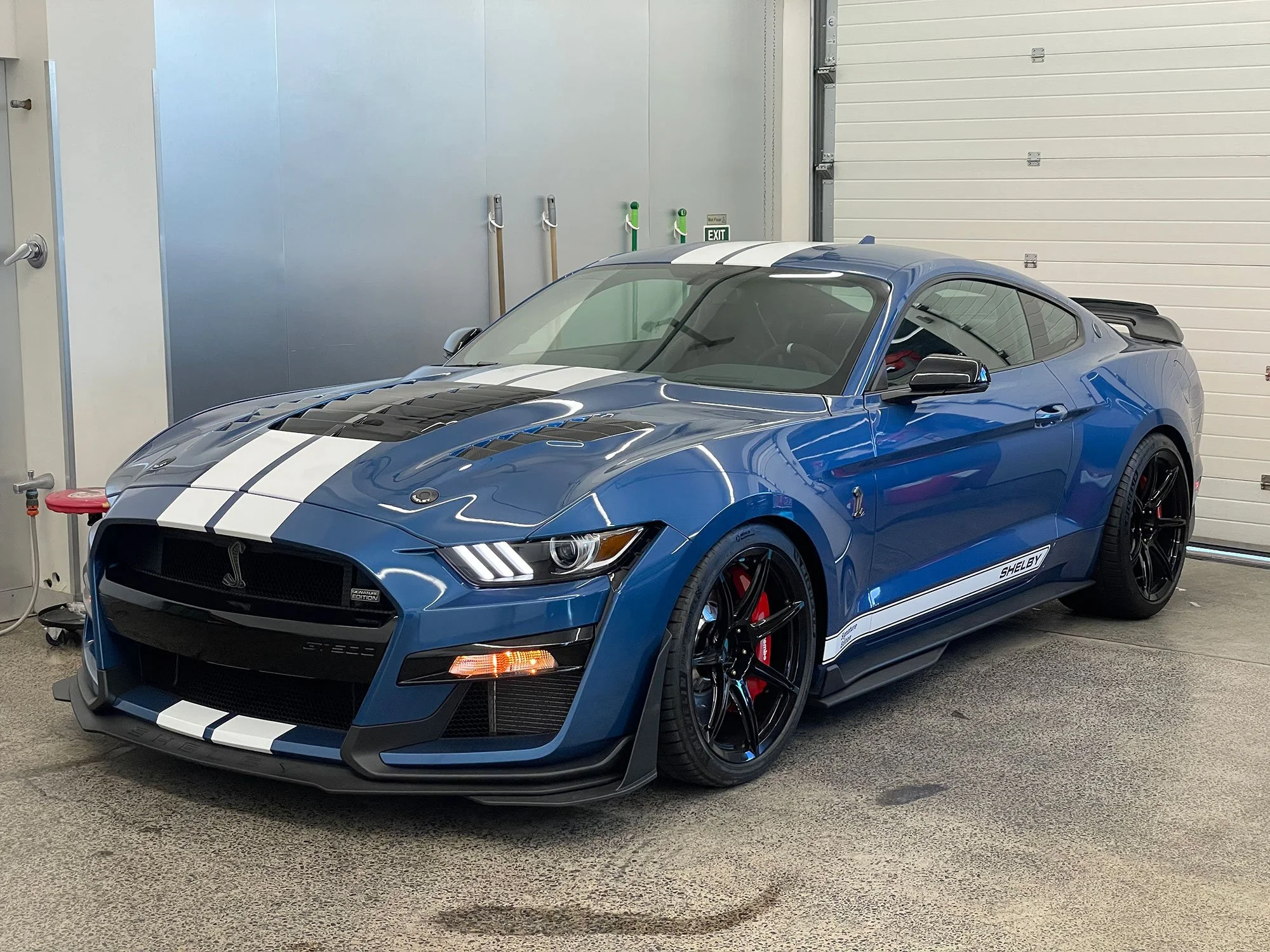 A blue Shelby GT500 Mustang with white racing stripes parked inside a garage.