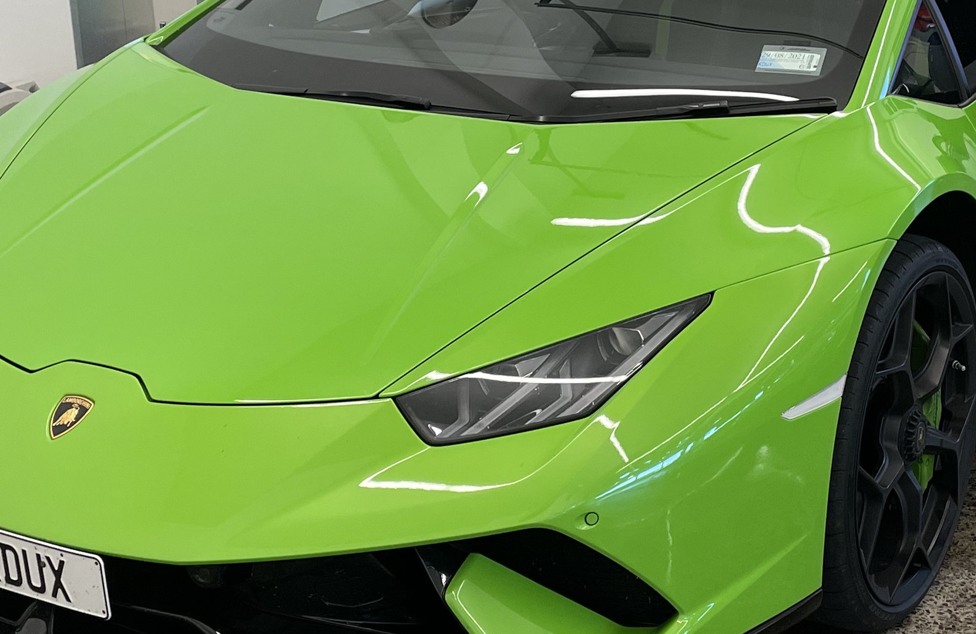 Front view of a bright green Lamborghini sports car with a black wheel, displayed indoors.