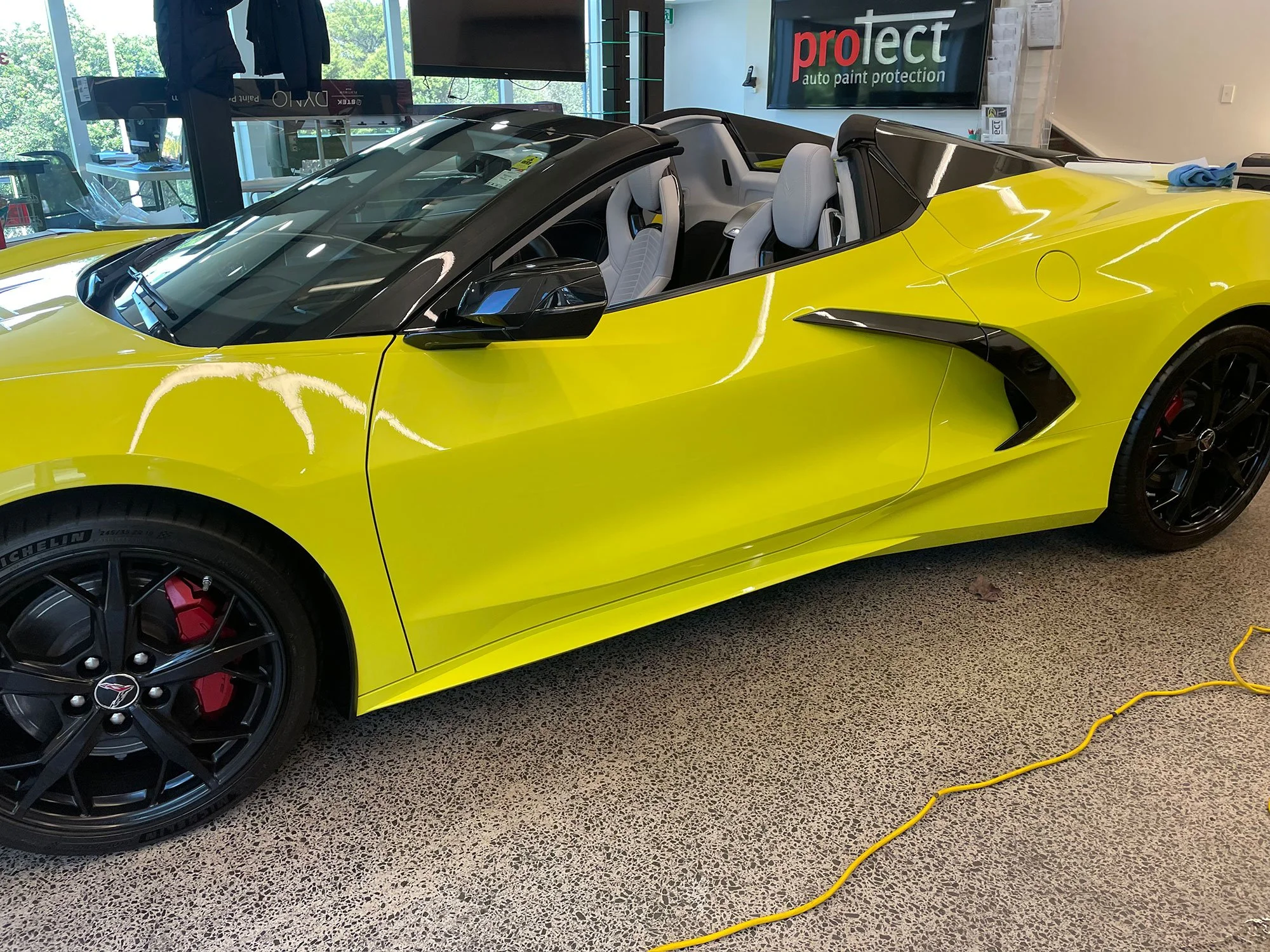 A bright yellow convertible sports car with black wheels and red brake calipers in an indoor showroom.