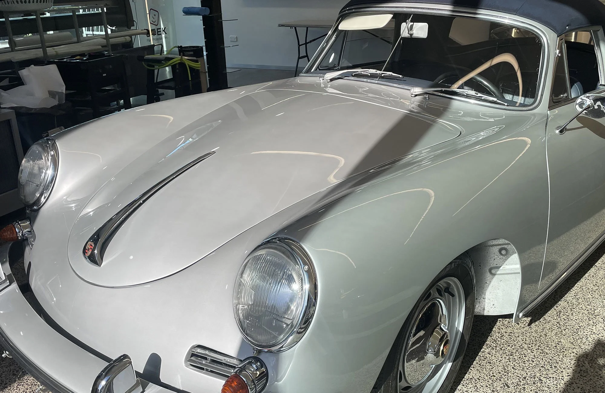 A classic silver Porsche 356 convertible sports car parked indoors with a black roof, showing the front and side view.