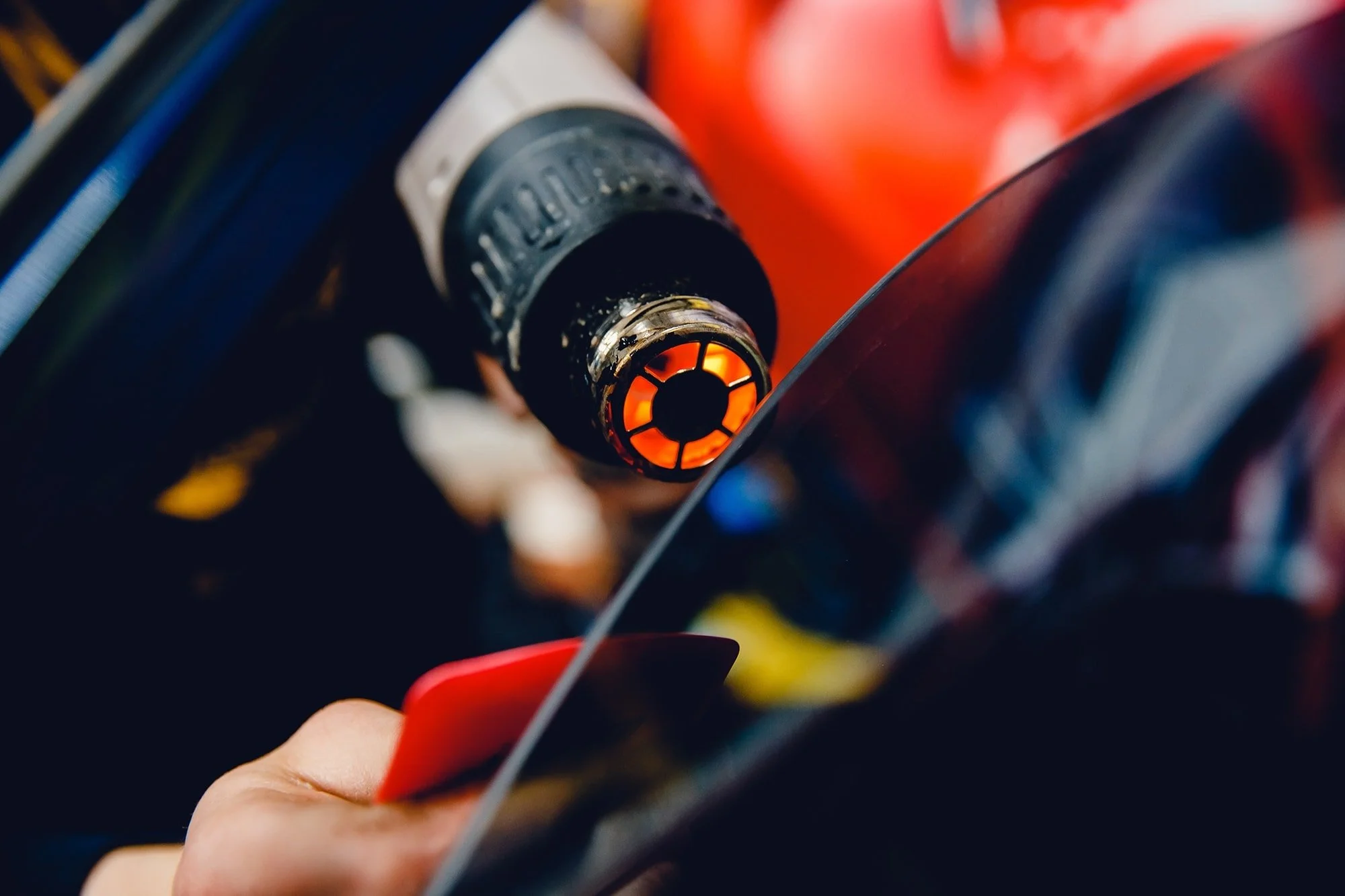 Close-up of a shining orange and black spark plug in a car engine, with a person's hand holding a red tool nearby.