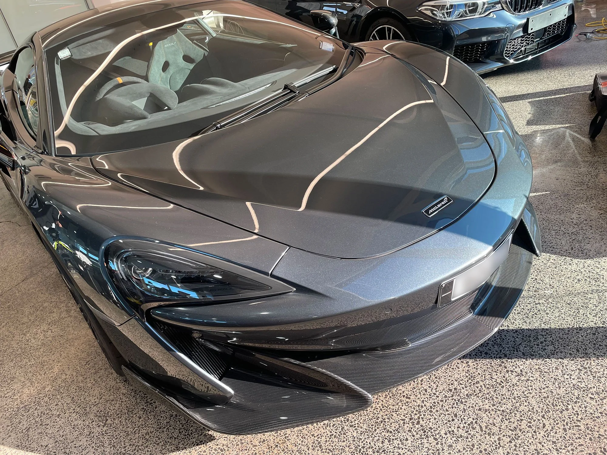 A gray McLaren sports car with a sleek design, low profile, and carbon fiber accents parked indoors.