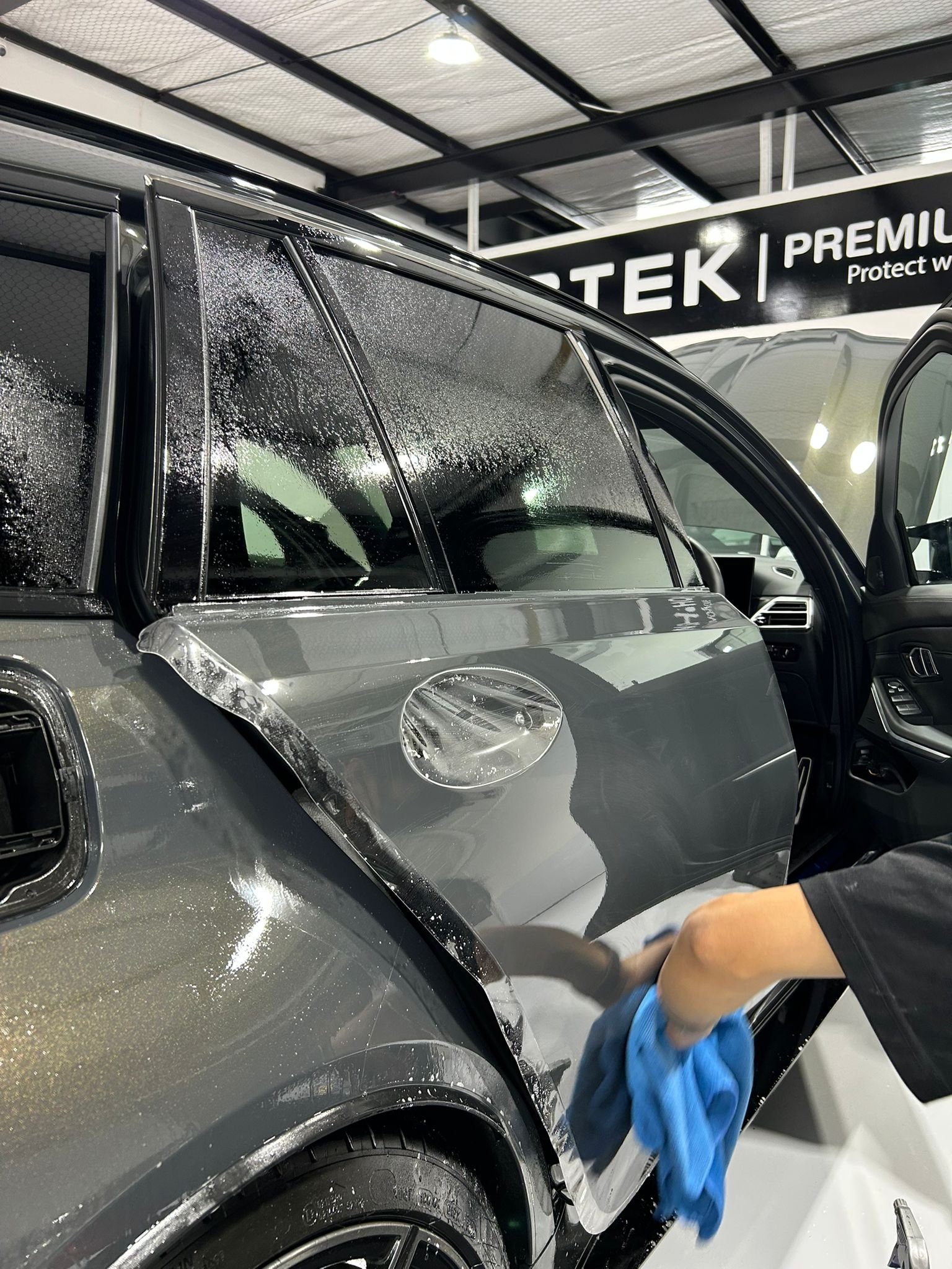 Car detailing in progress, with a person cleaning the side mirror of a gray vehicle inside a service center.