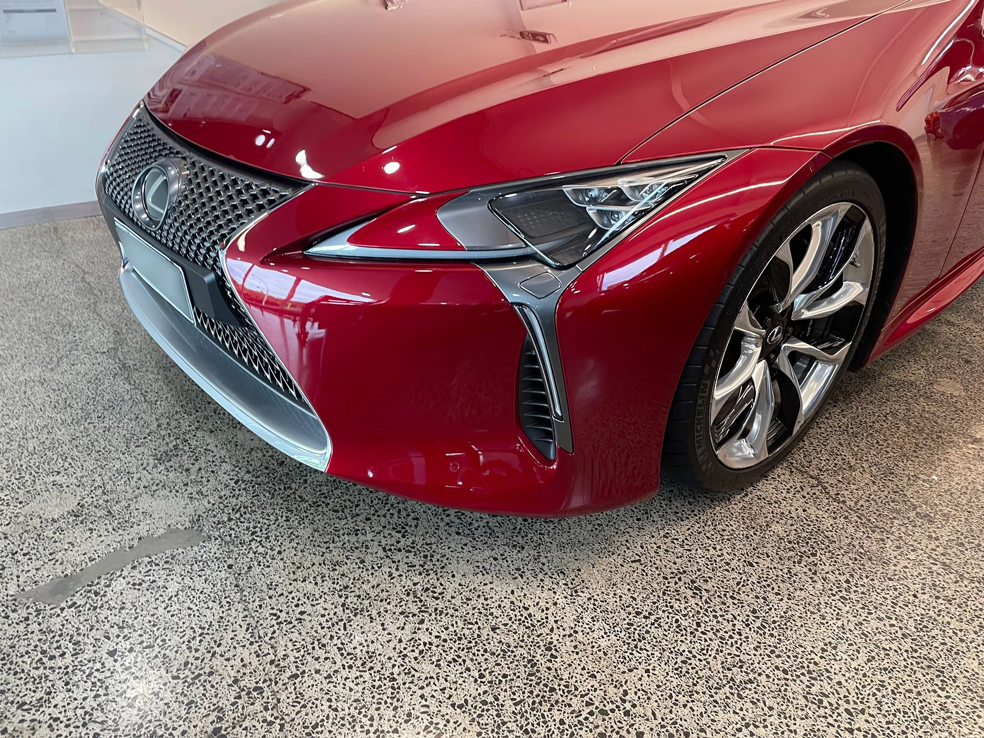Red luxury car with sleek design, chrome grille, and sporty alloy wheels parked indoors.