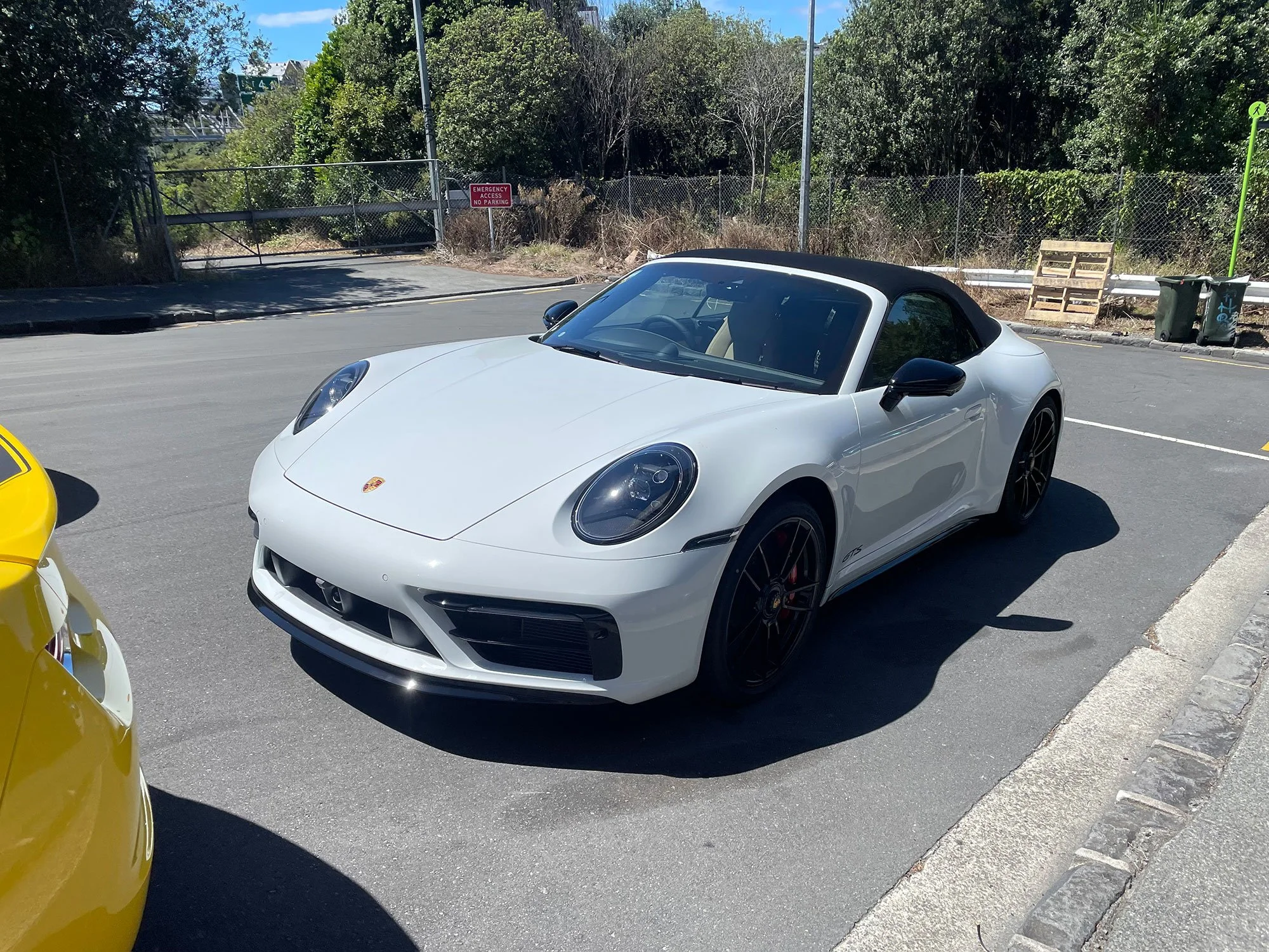 A white Porsche 911 convertible with black wheels parked in a parking lot on a sunny day.