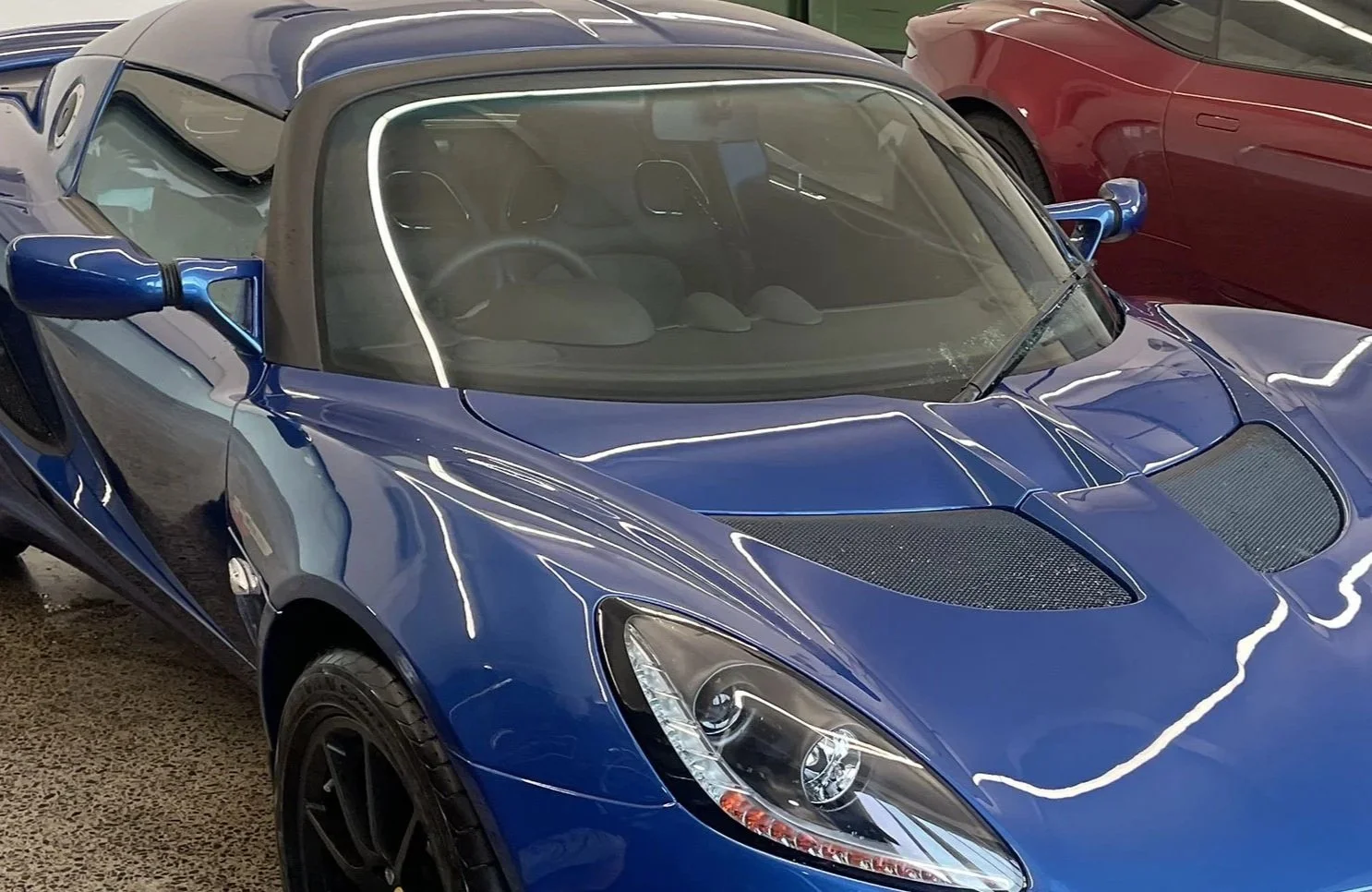 A blue sports car with a black convertible soft top, parked indoors among other cars.