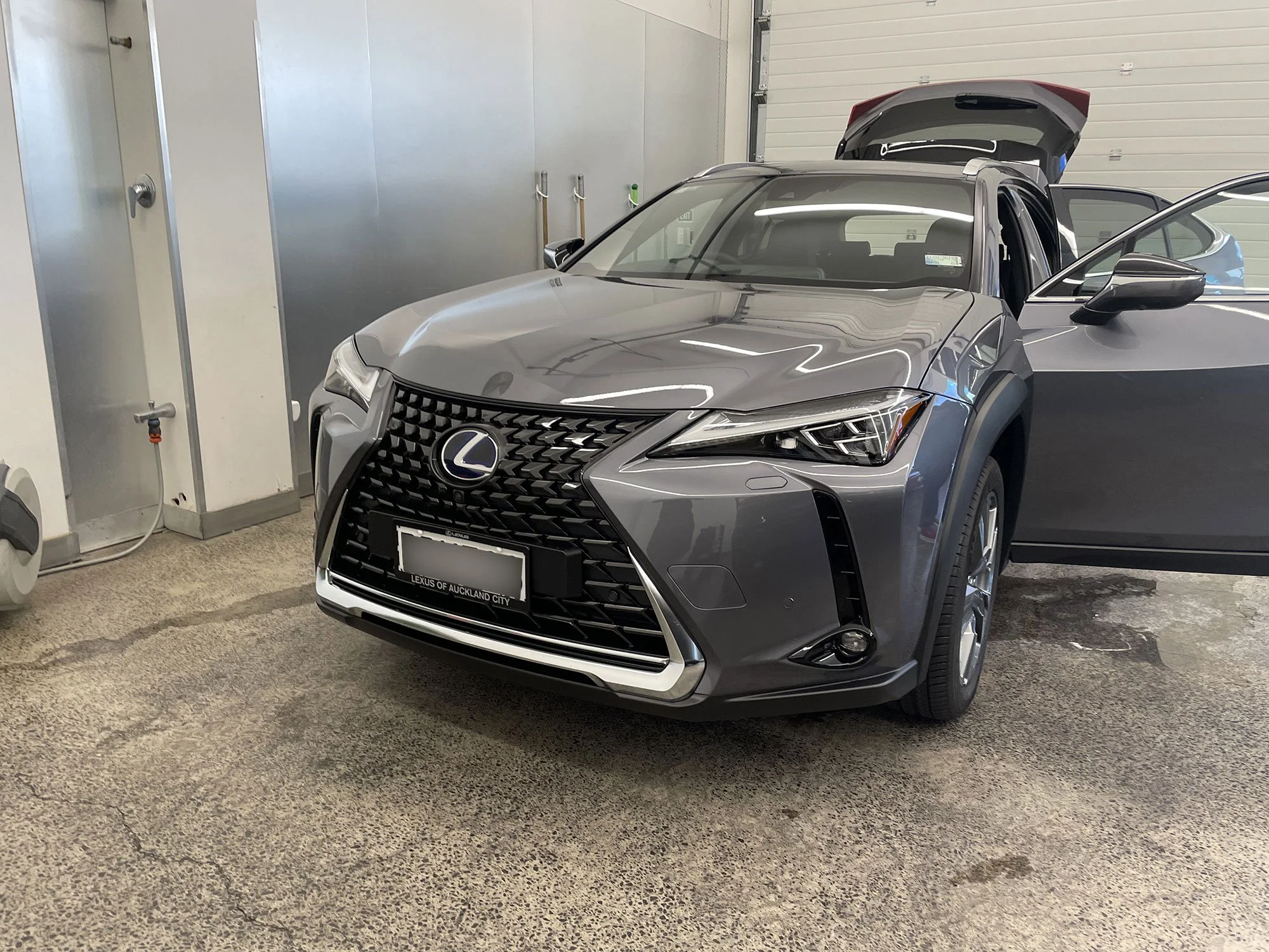 Gray Lexus SUV parked inside a garage, with front driver-side door open and rear hatch raised.
