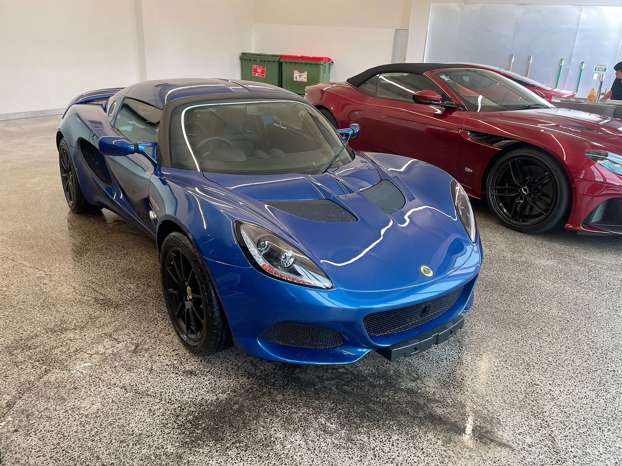 A blue Lotus sports car with black wheels parked indoors next to a red sports car.