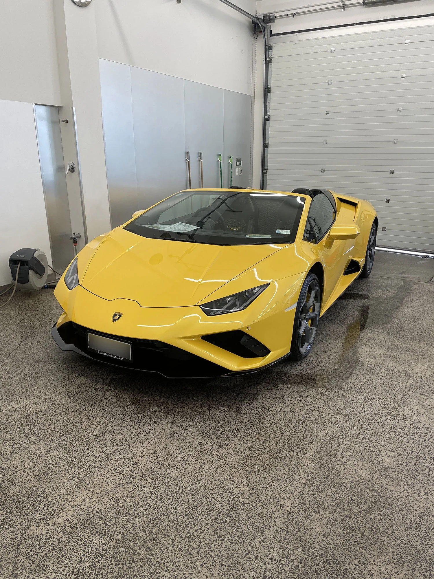 Yellow Lamborghini sports car parked inside a garage with an industrial-style floor and a white roll-up door.