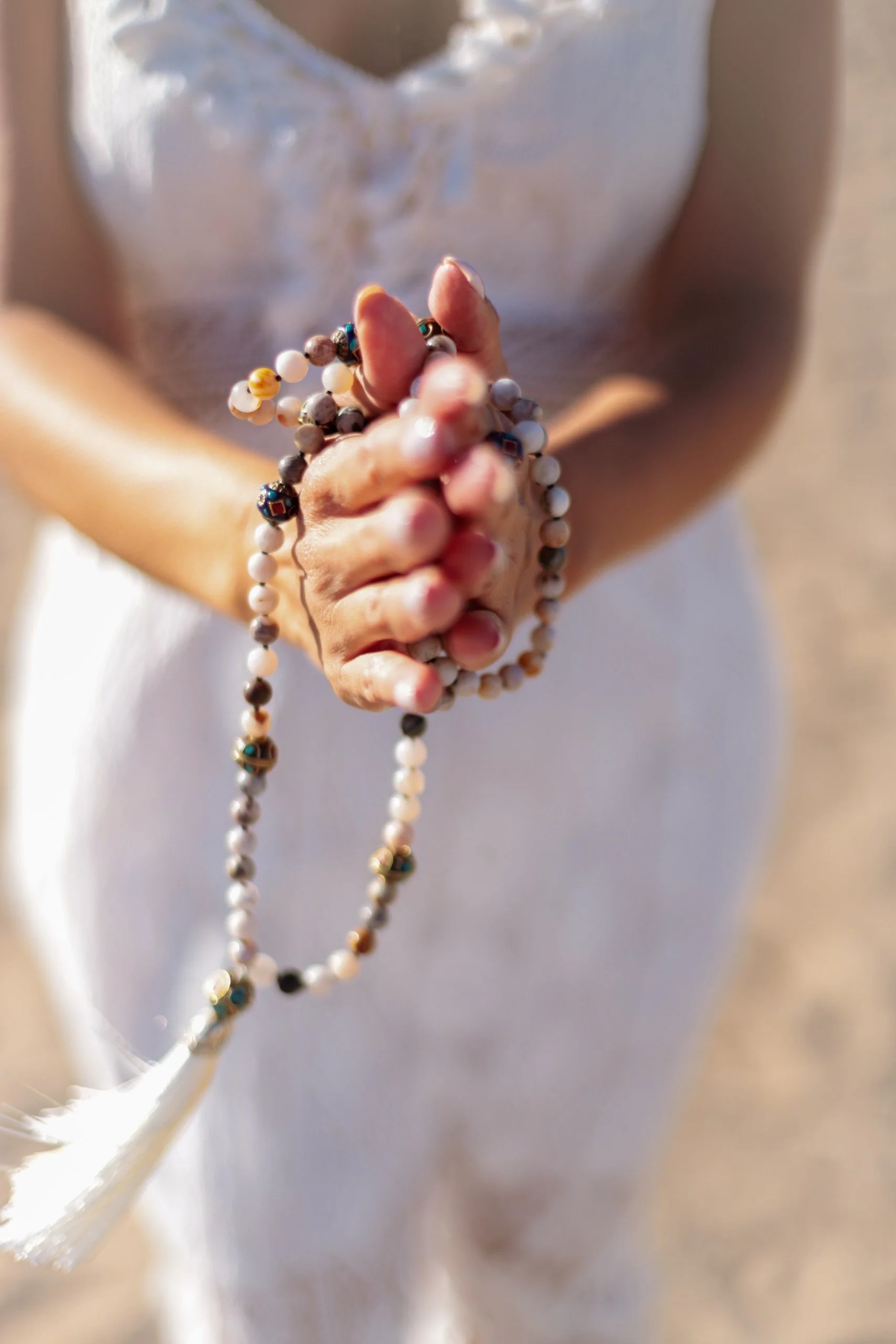 Person holding prayer beads or rosary, wearing a white dress.