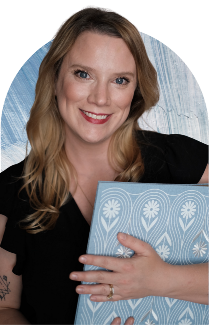 A woman with long blonde hair, blue eyes, and fair skin, smiling and holding a blue and white patterned folder. She is wearing a black top and a gold ring, with a light blue textured background.
