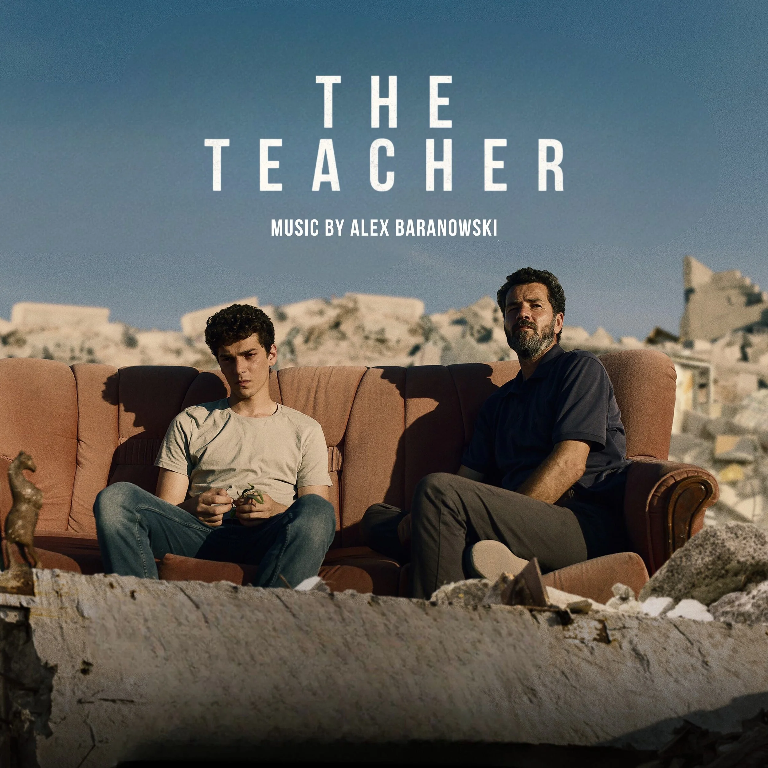 A man and a teenager sitting on a brown sofa outdoors, with a rocky landscape and blue sky in the background, poster for a film titled 'The Teacher' with music by Alex Baranowski.
