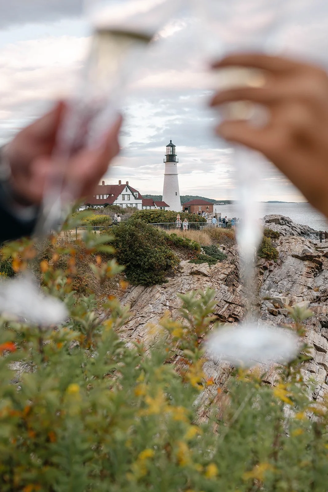 newly engaged couple celebrating with champagne overlooking a lighthouse in maine