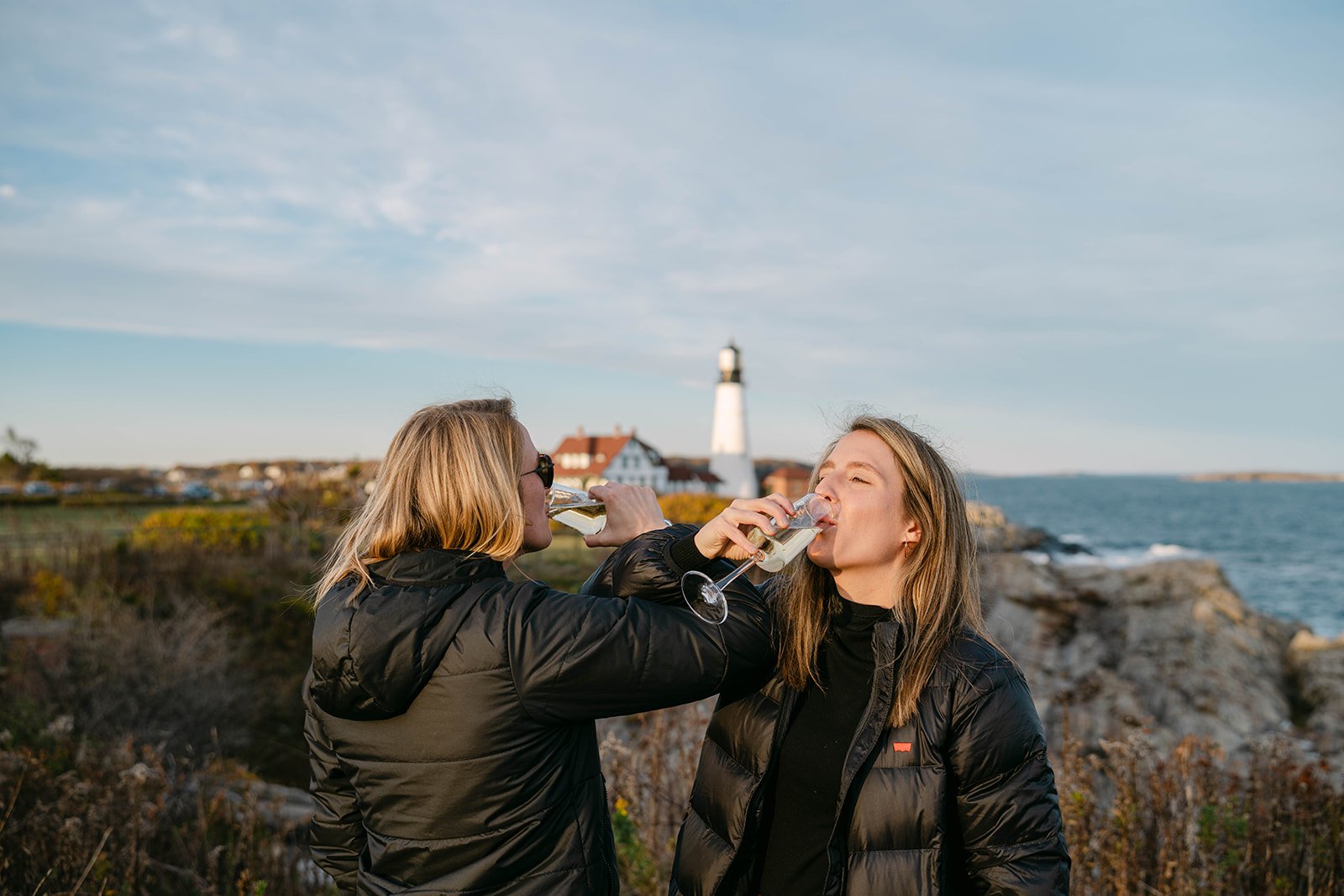 newly engaged couple celebrating with champagne overlooking a lighthouse in maine