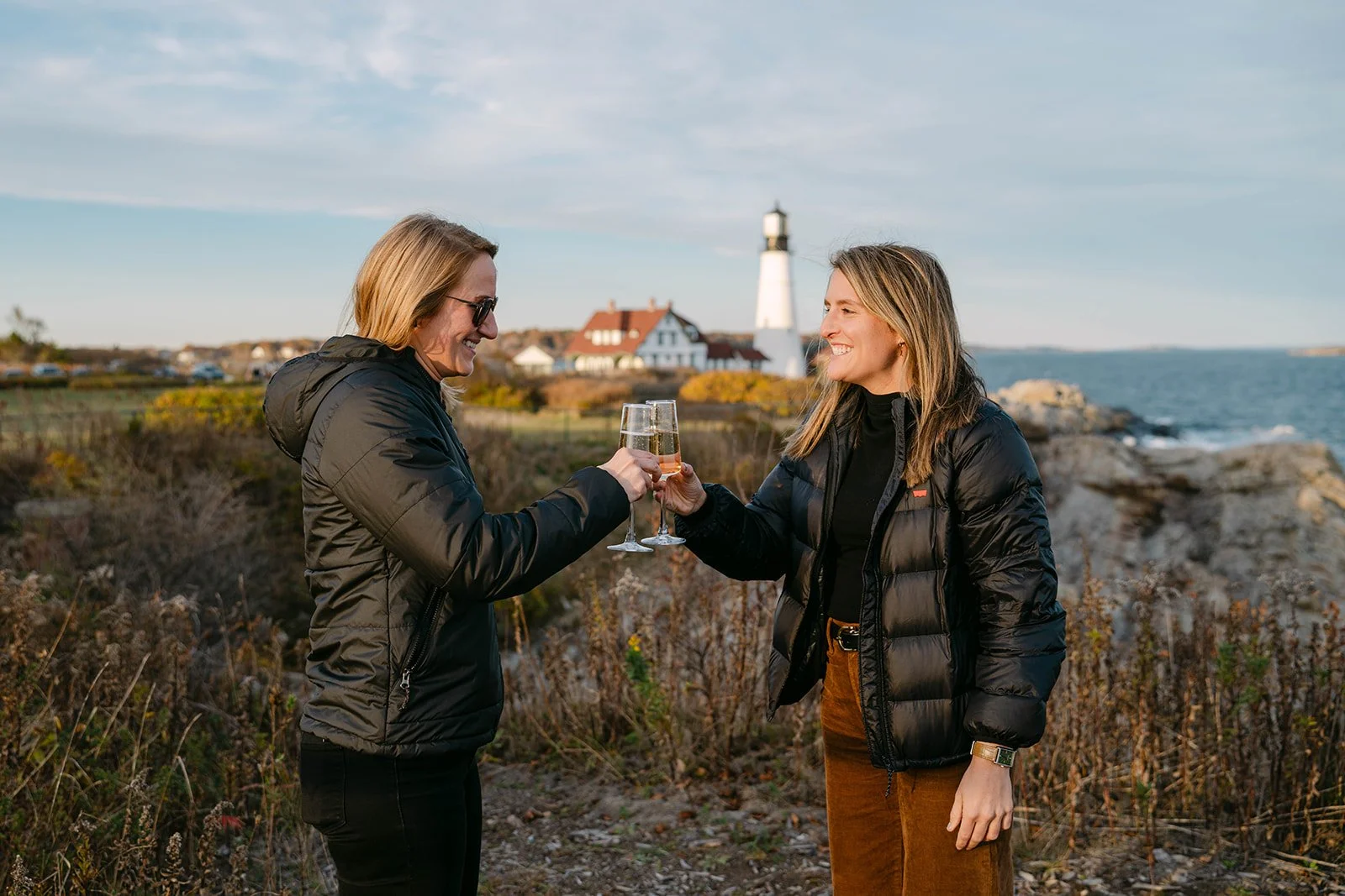 newly engaged couple celebrating with champagne overlooking a lighthouse in maine