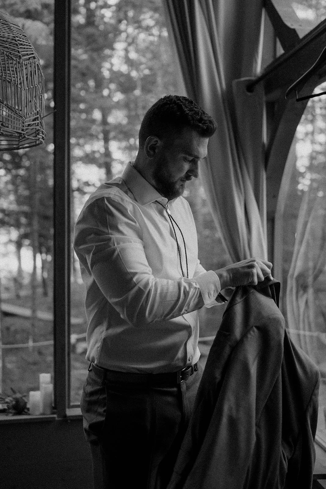 groom getting ready in front of a large lakeside cabin window