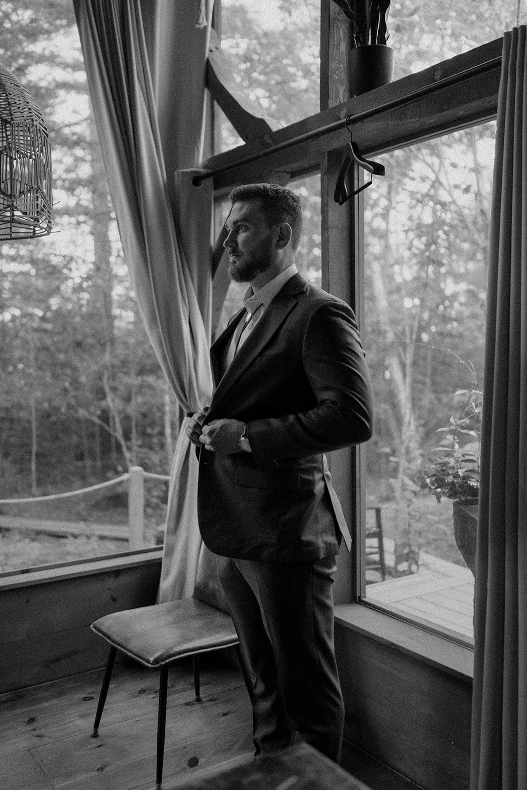 groom getting ready in front of a large lakeside cabin window