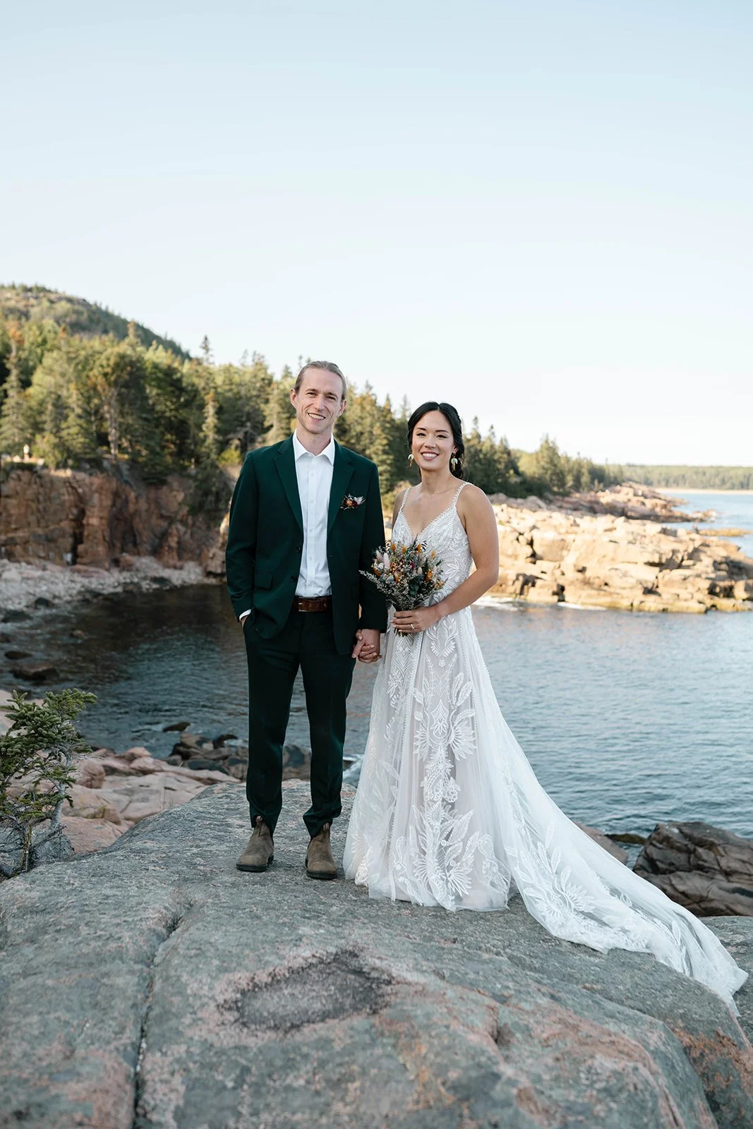 bride and groom standing on a cliff at monument cove during their acadia elopement