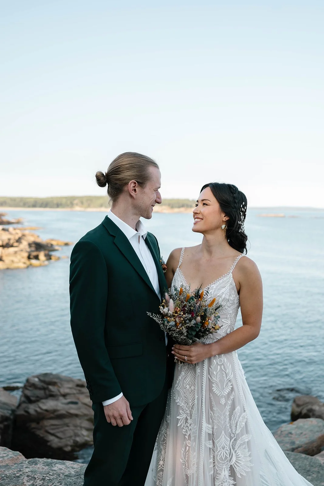 bride and groom standing on a cliff at monument cove during their acadia elopement