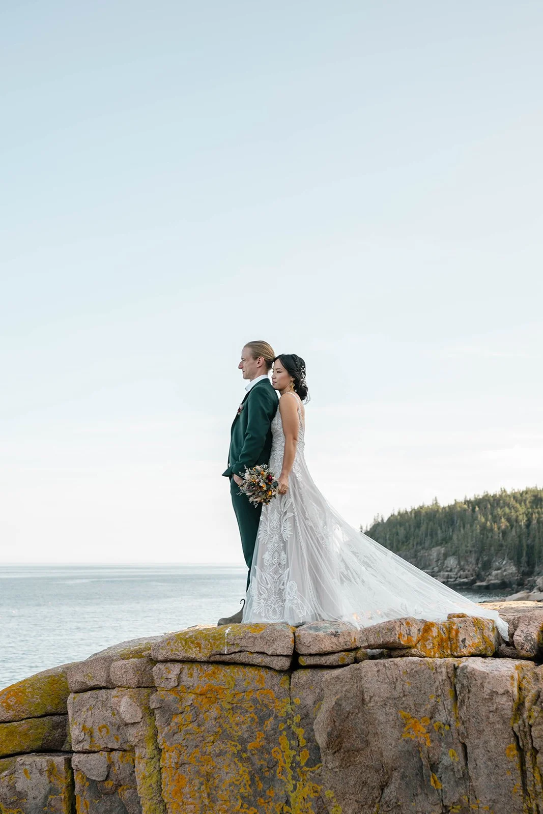 bride and groom standing on a cliff during their acadia elopement