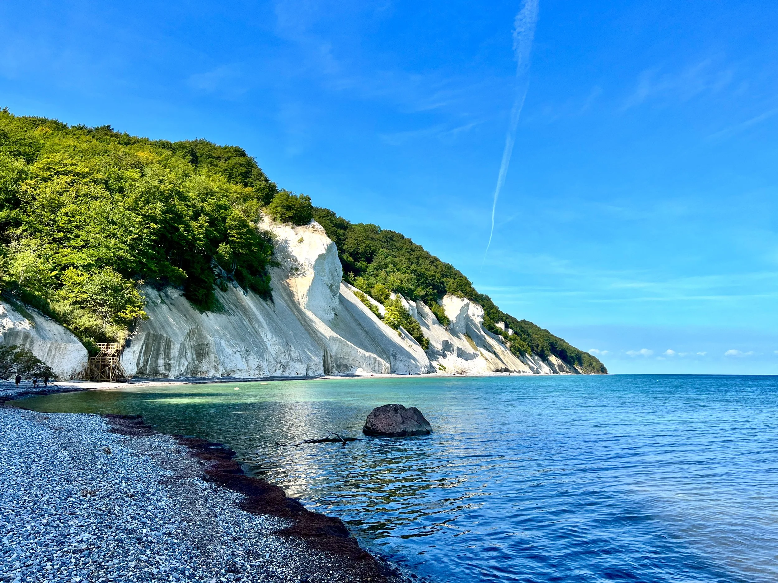 White chalk cliffs along a green hillside next to a calm blue sea on a sunny day with a clear sky