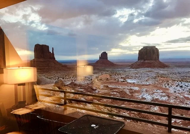 Interior view of a room with a large window showing Monument Valley's mesas and desert landscape during sunset.
