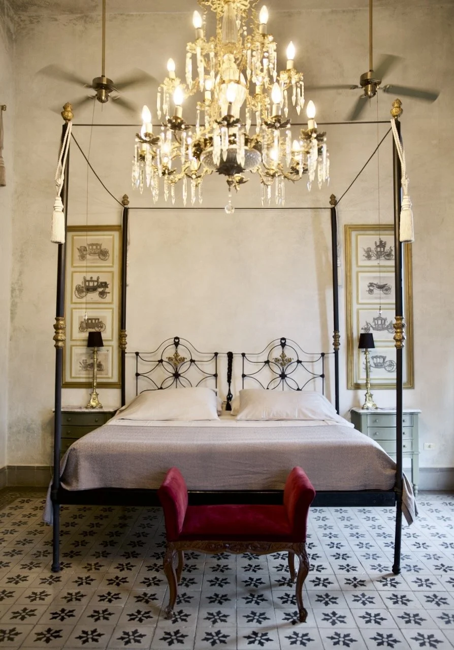 The elegant bedroom of Coqui Coqui Merida with a canopy bed, chandelier, and vintage decor including framed pictures and antique furniture.