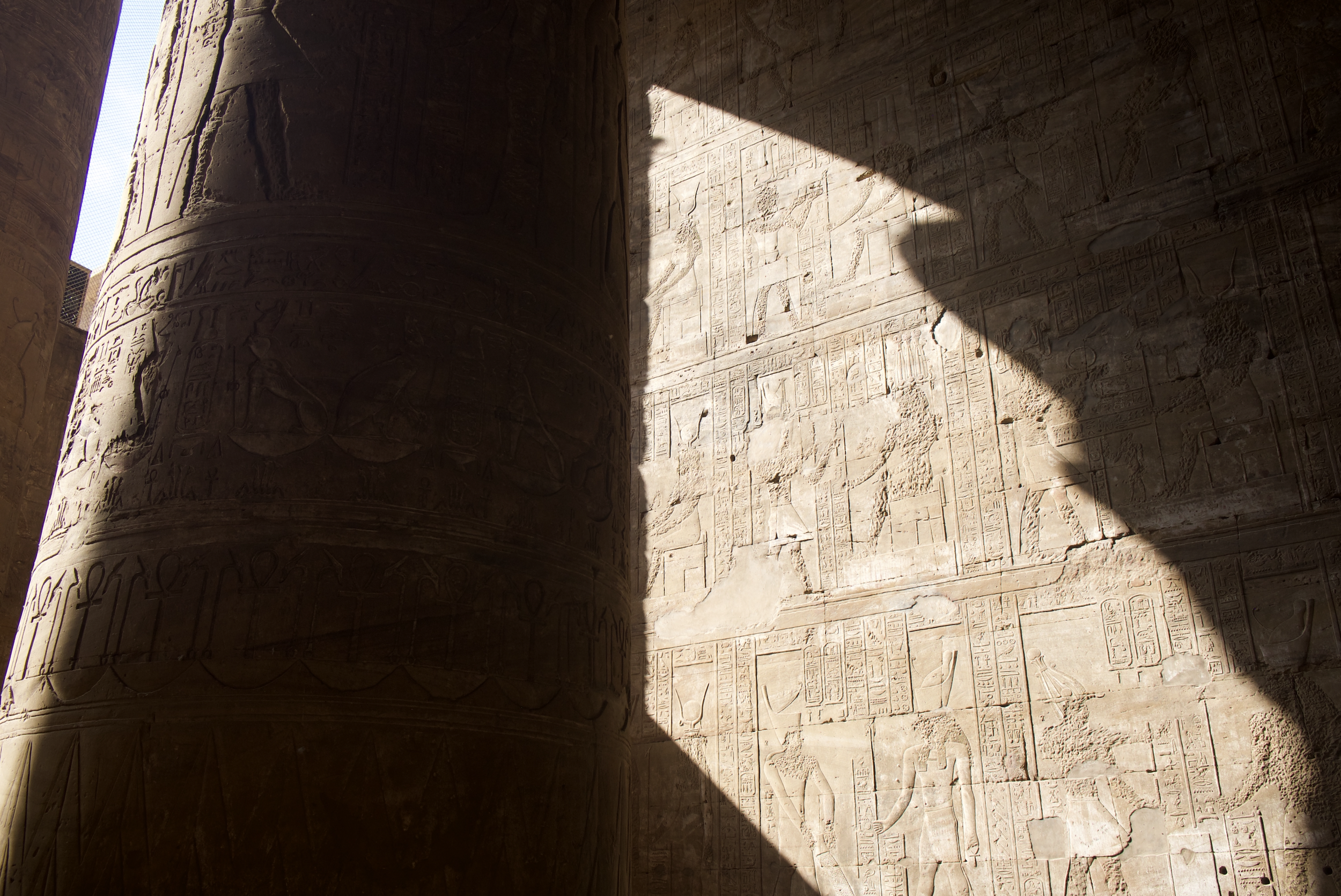 Ancient Egyptian hieroglyphic carvings on a temple wall with dramatic diagonal shaft of light, Luxor — ALTEZA Journal