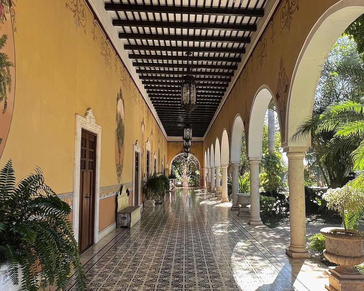 Colonnaded corridor of a historic hacienda in Mérida, Mexico, with painted ochre walls, ornate tiled floors and repeating arches — ALTEZA luxury travel advisory