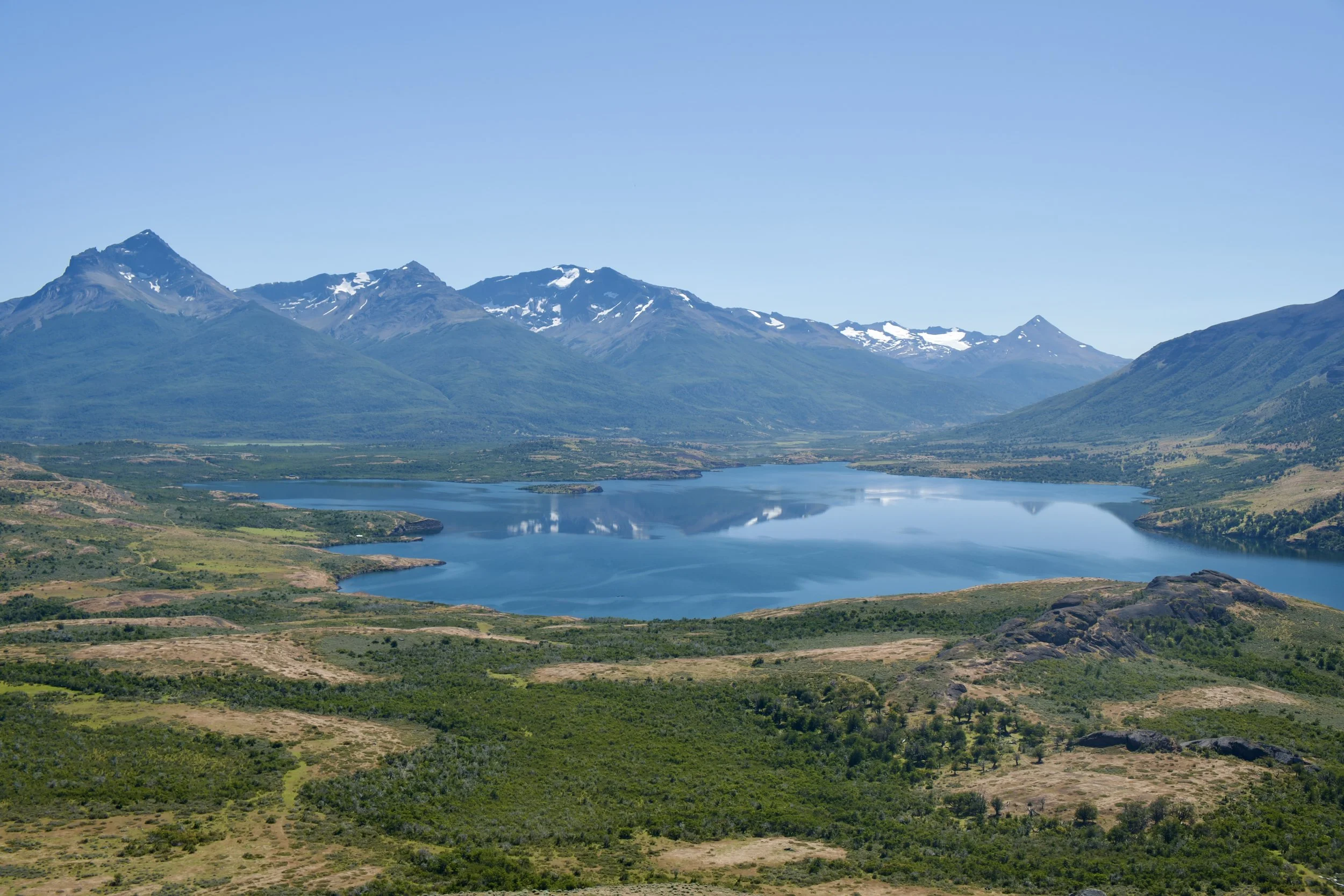 Vast Patagonian lake surrounded by snow-dusted mountains and native forest under a clear blue sky — ALTEZA Journal